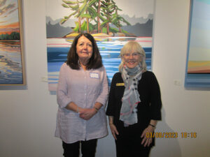 Two women standing in front of a painting.